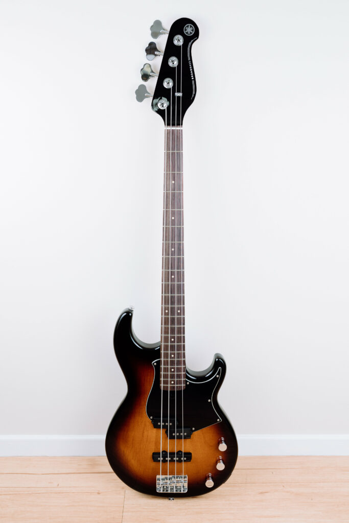 A photo of a Yamaha BB-343 bass guitar propped up against the wall. The body fades from black around the edges into a dark rich orange/red wood in the middle